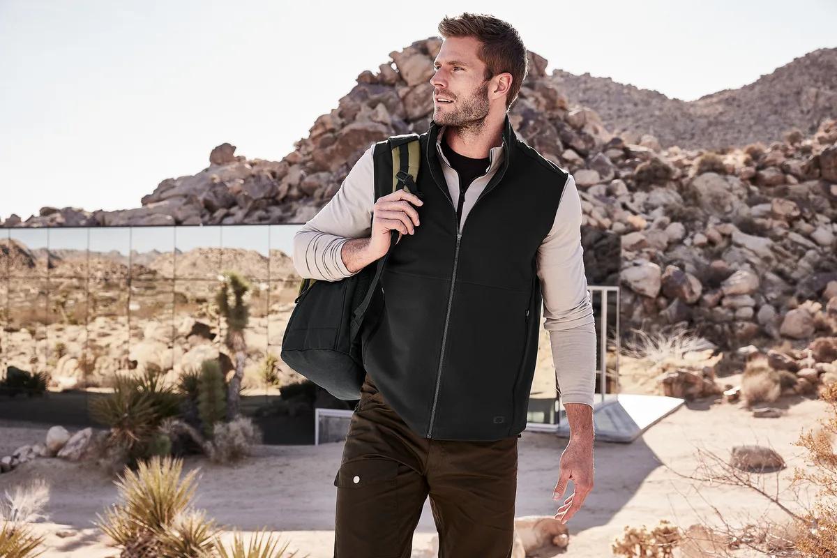 Man in an OGIO soft shell vest carrying an OGIO duffel in the desert